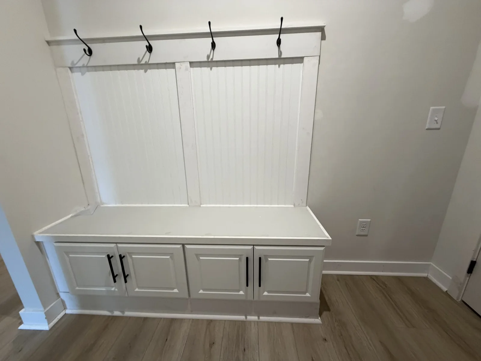 White entry bench with cabinet storage, paneled back and coat hooks